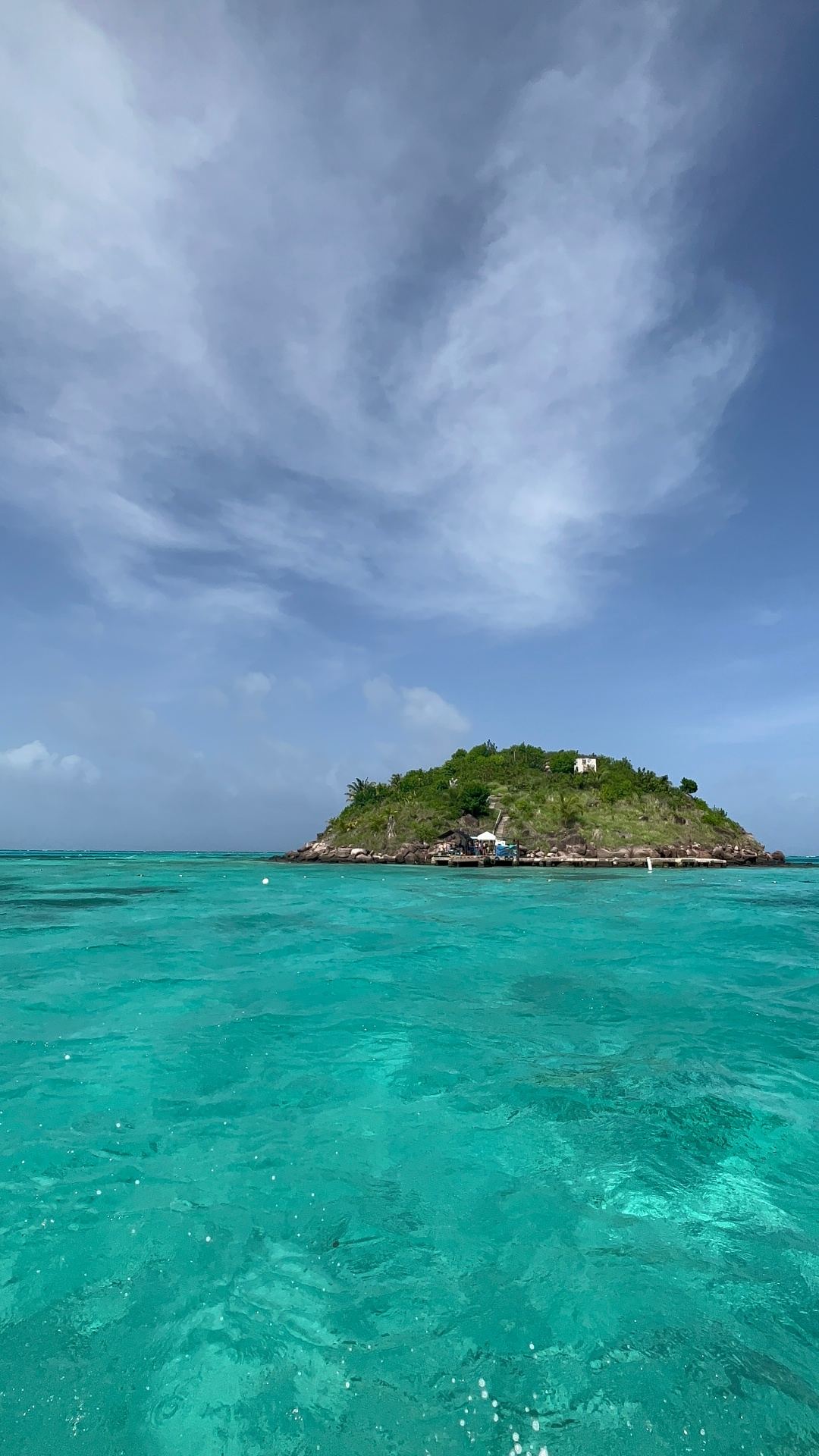 A small green islet rising out of turquoise water under a wide Caribbean sky